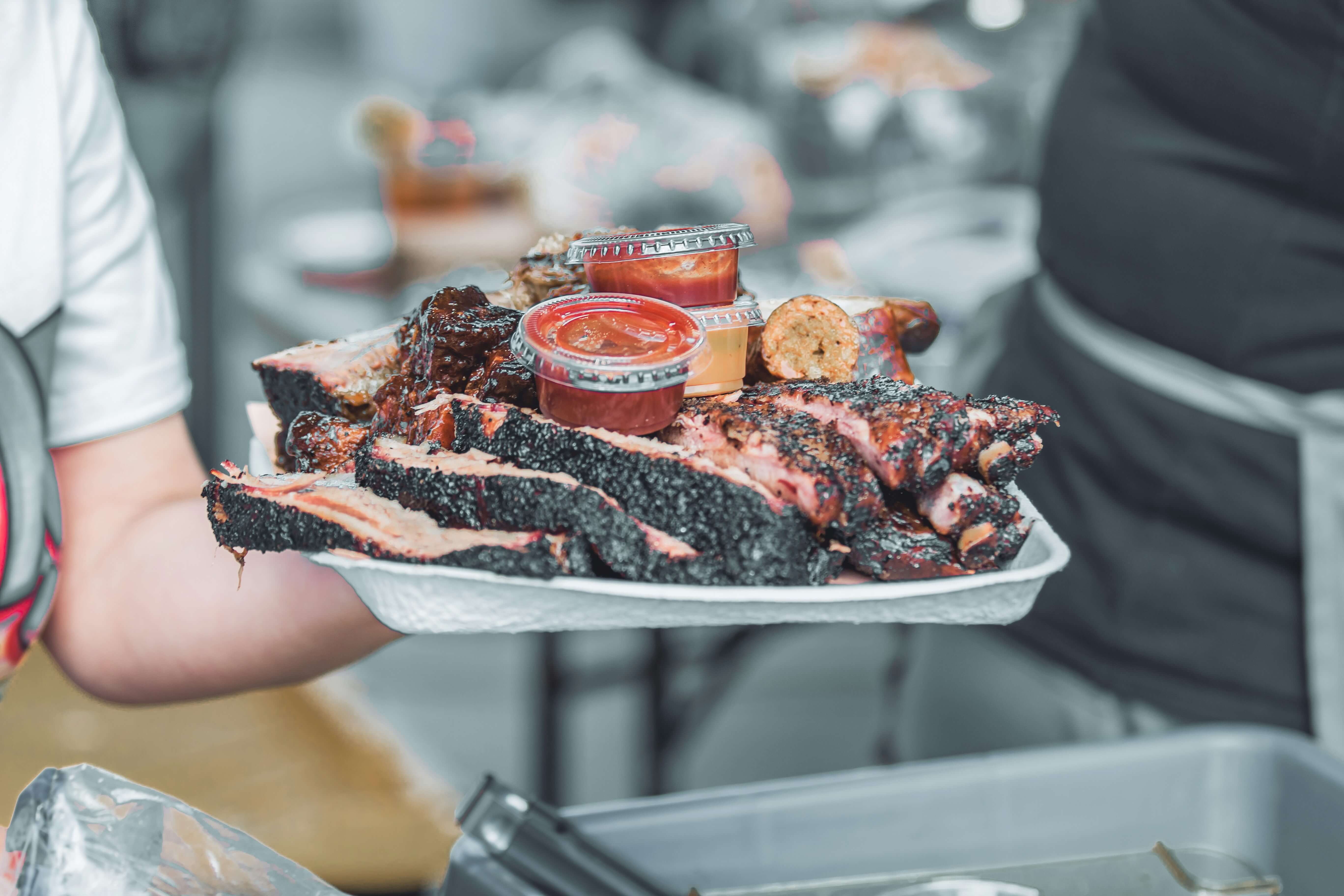 A tray of sliced beef brisket, with a selection of take away sauces.